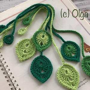 May include: A handmade crochet bookmark featuring a leaf design in shades of green. The bookmark is placed on an open book with botanical illustrations. The text "(c) Olga Poltava" is visible in the upper right corner.