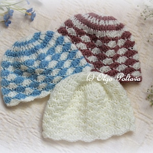 May include: Three handmade crochet baby hats in soft colours. One is light blue and white with a diamond pattern, another is white, and the third is burgundy and white. The hats are displayed on a white surface with floral accents.