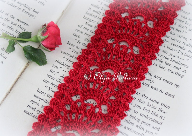 May include: A close-up of a red crocheted bookmark with a delicate floral pattern. The bookmark is lying on a book with text that reads "(c) Olga Poltava".