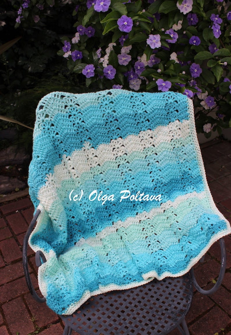 May include: A handmade crochet blanket in shades of blue and white, draped over a metal chair. The blanket features a wavy pattern and is made with soft yarn. The text "(c) Olga Poltava" is visible on the blanket.