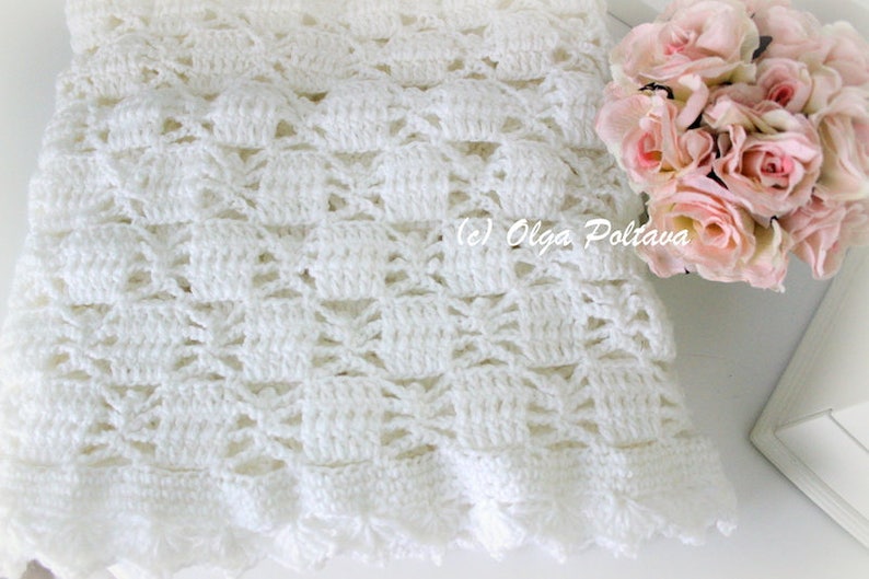 May include: A white crocheted blanket with a detailed openwork pattern. The blanket has a scalloped edge and is next to a bouquet of pink roses. The text "(c) Olga Poltava" is visible.