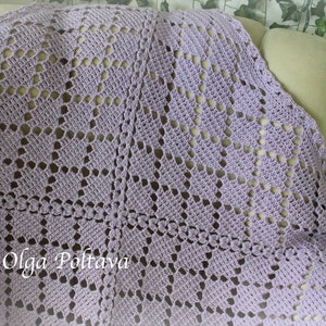 Puede incluir: Una manta de crochet de color lavanda con un delicado patr&oacute;n de calado. La manta est&aacute; colocada sobre un sof&aacute; beige claro.