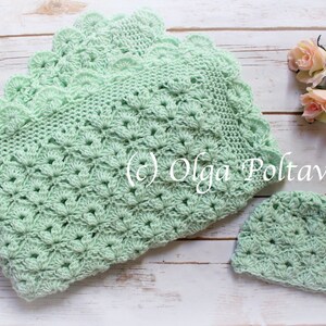 May include: A mint green crochet baby blanket and matching hat set. The blanket features a scalloped edge and a detailed floral pattern. The set is displayed on a light wood surface, with a few pink roses in the background. The text "(c) Olga Poltava" is visible.