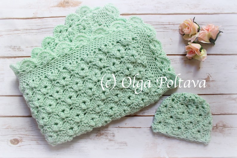 May include: A mint green crochet baby blanket and matching hat set. The blanket features a scalloped edge and a detailed floral pattern. The set is displayed on a light wood surface, with a few pink roses in the background. The text "(c) Olga Poltava" is visible.