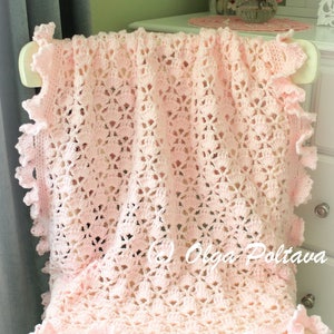 May include: A pink crocheted baby blanket with a delicate lace pattern and ruffled edges. The blanket is draped over a white chair.