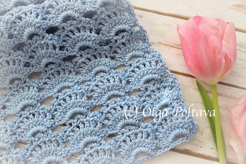 May include: A light blue crocheted fabric with a repeating pattern of scallops. The fabric is laid on a white wooden surface with a pink tulip in the background. The text (c) Olga Poltava is visible in the lower right corner of the image.
