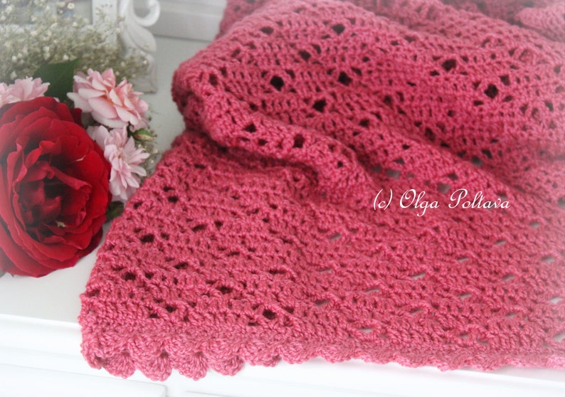 May include: A close-up of a pink crocheted shawl with a scalloped edge. The shawl is made with a delicate stitch pattern and has a soft, feminine look.
