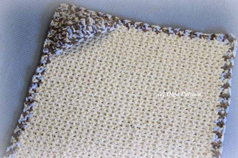 May include: A crocheted baby blanket in cream with a brown and blue border.