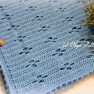 Puede incluir: Una manta de beb&eacute; de ganchillo azul claro con un delicado patr&oacute;n de punto abierto. La manta est&aacute; hecha de hilo suave y tiene una textura sutil.