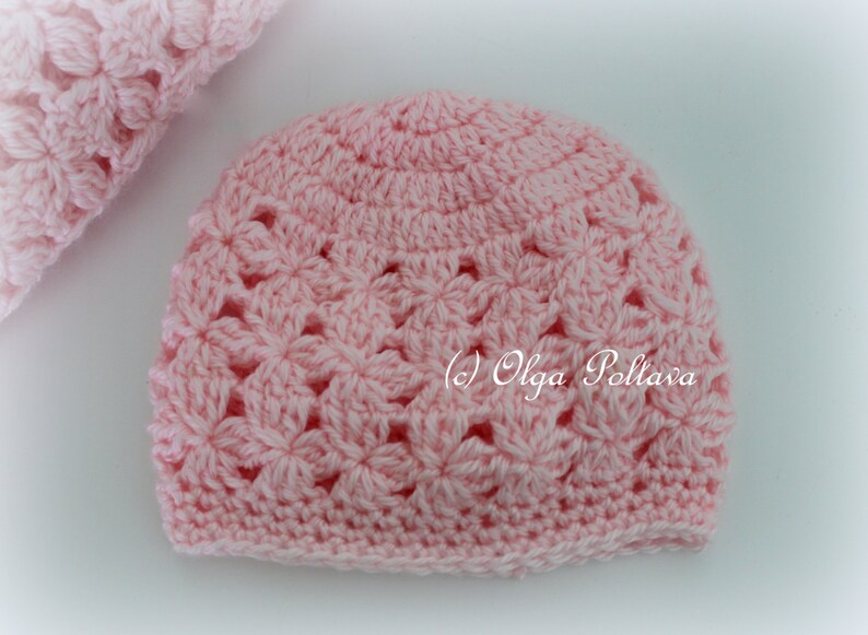 May include: A pink crocheted hat with a flower pattern. The hat is made with a soft yarn and has a comfortable fit.
