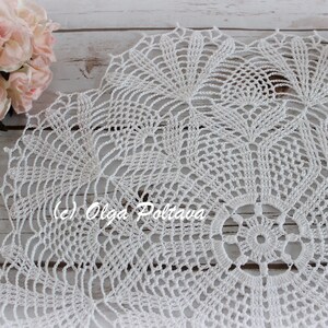 May include: White crocheted doily with a delicate, intricate design. The doily has a circular shape and features a central motif with radiating patterns.