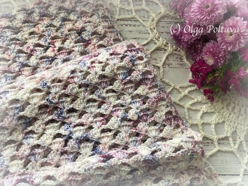 Pu&ograve; includere: Un scialle all'uncinetto di colore crema con accenti rosa e blu. Lo scialle &egrave; realizzato con un punto delicato e traforato e ha una texture morbida e fluida. (c) Olga Poltava