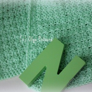 May include: A light mint green crocheted fabric with a textured stitch pattern and a solid lime green wooden letter N placed on top. The text (c) Olga Poltava is printed in white on the fabric surface, which features a soft, woven appearance.