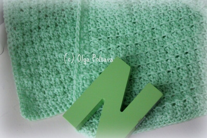 May include: A light mint green crocheted fabric with a textured stitch pattern and a solid lime green wooden letter N placed on top. The text (c) Olga Poltava is printed in white on the fabric surface, which features a soft, woven appearance.