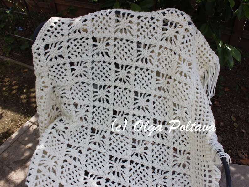 May include: A white crocheted throw blanket with a delicate pineapple stitch pattern. The blanket has a fringe border and is draped over a chair.