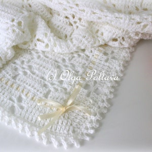 May include: White crocheted baby blanket with a delicate lace pattern and a cream-colored satin ribbon tied in a bow. The blanket is on a white surface with pink roses.