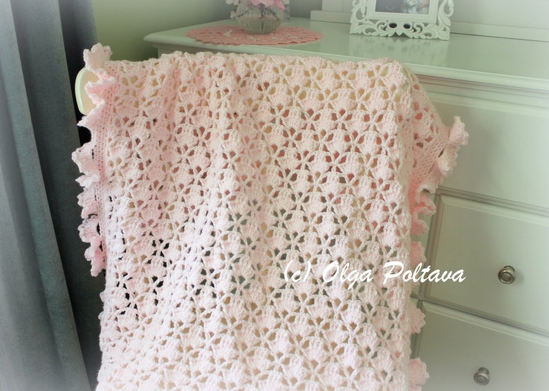 May include: A pink crocheted baby blanket with a delicate floral pattern and a scalloped edge.