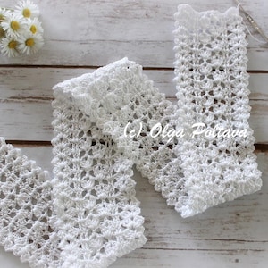 May include: A white crocheted scarf featuring an intricate, repeating openwork pattern with a scalloped edge. The long, rectangular accessory is crafted from fine white yarn and displays a delicate, airy texture throughout its entire length.