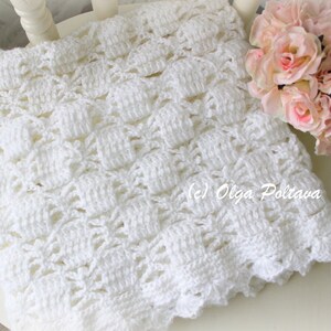 May include: A handmade white crochet blanket with a textured pattern, resting on a white chair. The blanket has a scalloped edge and is accompanied by a bouquet of pink roses. The copyright text "(c) Olga Poltava" is visible.