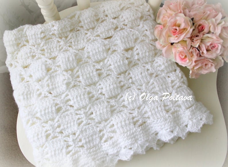 May include: A handmade white crochet blanket with a textured pattern, resting on a white chair. The blanket has a scalloped edge and is accompanied by a bouquet of pink roses. The copyright text "(c) Olga Poltava" is visible.
