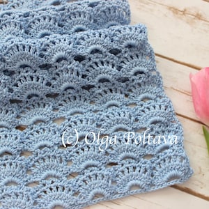 May include: A light blue crocheted scarf with a delicate, lacy pattern. The scarf is laid out on a white wooden surface with two pink tulips.