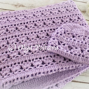 May include: A lavender crochet baby blanket and matching hat. The blanket has a delicate, lacy pattern and is folded in half. The hat is small and sits on top of the blanket.