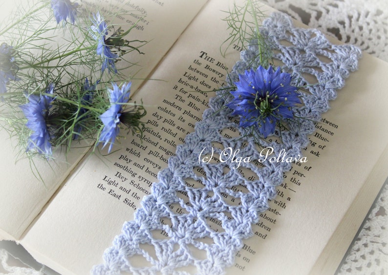 May include: A blue crocheted lace bookmark with a delicate floral pattern, resting on an open book with blue flowers. The text on the book reads "THE Blue the Bowery between the t Light does bric-a-brae, it for pain-ki The Blue modern pharm colates its on day pills are r pills rolled ou patula, rolle calcined magu board pill-bos which coveys play and beco soothing syrup Ikey Schoen Light and the East Side, "