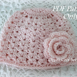 May include: A pink crocheted hat with a matching flower embellishment. The hat is made with a delicate stitch pattern and has a soft, feminine look. The text "PDF Pattern Only" and "Olga's Crochet Frenzy" are visible in the image.