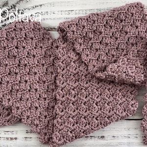 Puede incluir: Bufanda de ganchillo hecha a mano, de color malva, con un patrón de puntada texturizada. La bufanda está doblada y expuesta sobre una superficie de madera de color claro. La imagen incluye el texto "(c) Olga Poltava".