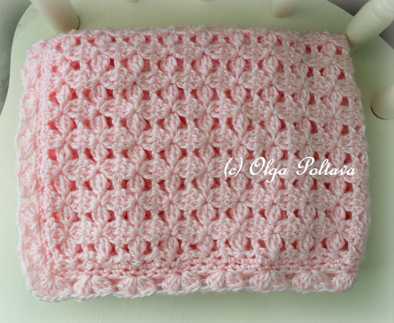 May include: A pink crocheted baby blanket with a delicate floral pattern. The blanket has a scalloped edge and is made with soft yarn.