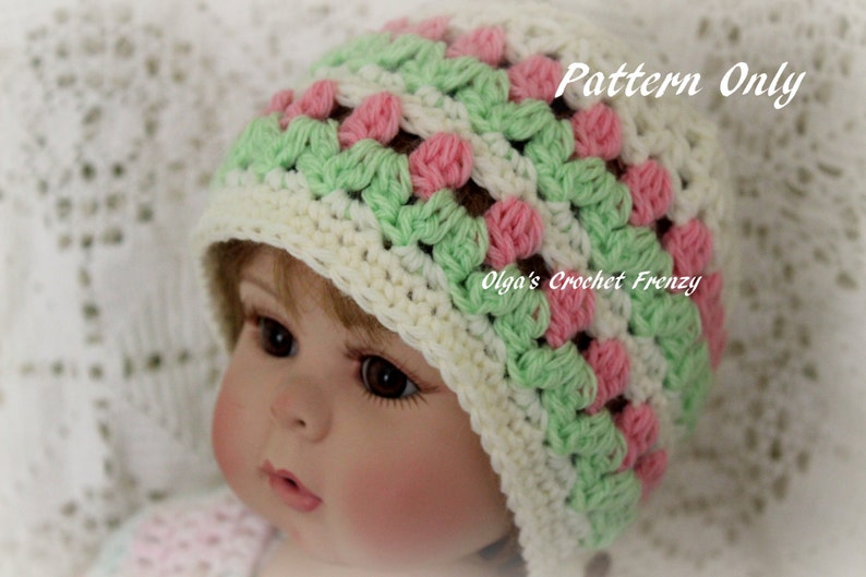 Puede incluir: Un gorro de beb&eacute; de ganchillo en crema, verde y rosa. El gorro presenta un dise&ntilde;o de granny square con el texto "Pattern Only" y "Olga's Crochet Frenzy". El gorro es para beb&eacute;s y ni&ntilde;os peque&ntilde;os.