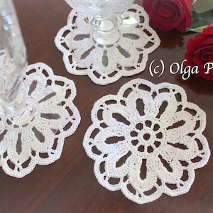 Puede incluir: Tres manteles individuales de ganchillo blanco con un delicado diseño floral. Los manteles individuales están sobre una superficie de madera con rosas rojas.