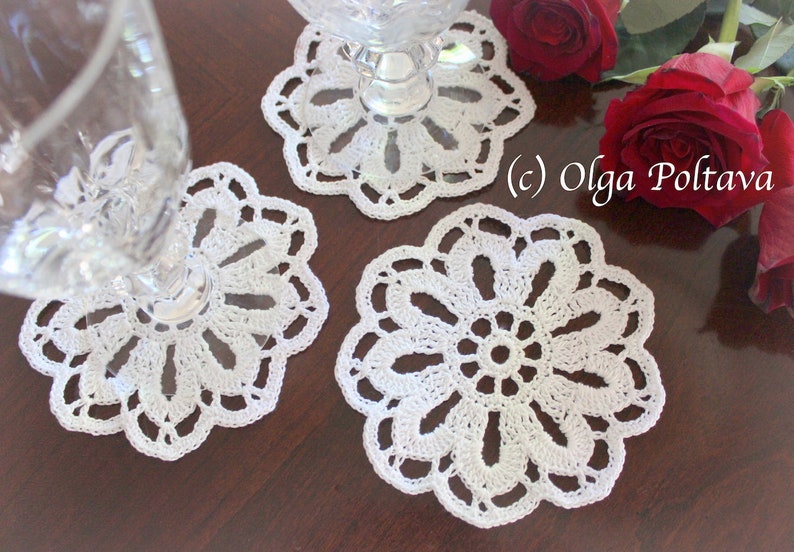 May include: Three white crocheted doilies with a delicate floral design. The doilies are on a wooden surface with red roses.