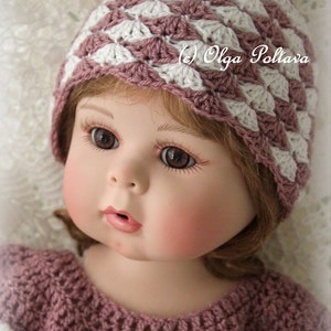 May include: A doll wearing a handmade crochet hat and dress. The hat features a shell stitch pattern in mauve and white. The dress is also mauve with white accents. The doll has brown eyes and rosy cheeks. The text "(c) Olga Poltava" is visible.