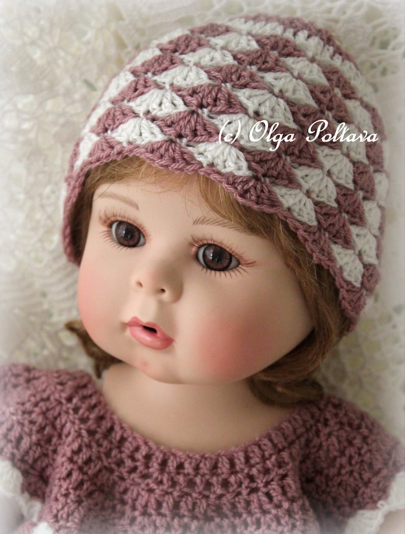 May include: A doll wearing a handmade crochet hat and dress. The hat features a shell stitch pattern in mauve and white. The dress is also mauve with white accents. The doll has brown eyes and rosy cheeks. The text "(c) Olga Poltava" is visible.