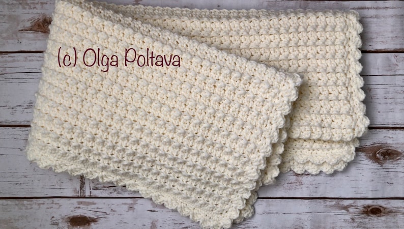Puede incluir: Una manta de beb&eacute; de ganchillo blanco con un borde festoneado. La manta est&aacute; doblada por la mitad y tiene un patr&oacute;n texturizado. El texto (c) Olga Poltava es visible en la imagen.