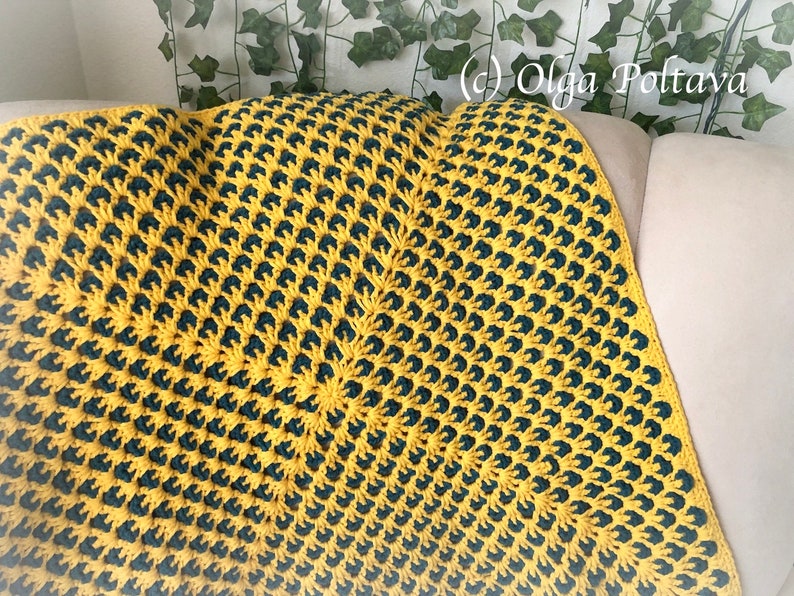 Puede incluir: Una manta de ganchillo con un patr&oacute;n amarillo y verde oscuro. La manta est&aacute; hecha con un patr&oacute;n de diamante repetido.