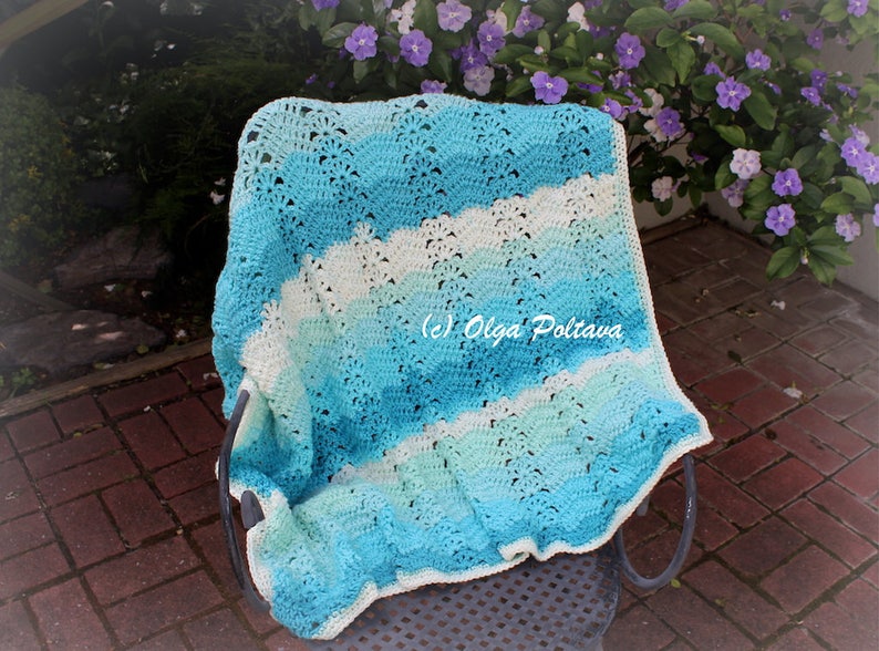 May include: A handmade crochet blanket in shades of blue and white, draped over a chair. The blanket features a wavy pattern and is made of soft yarn. The image includes the text "(c) Olga Poltava".