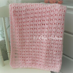 May include: A pink crocheted baby blanket with a delicate floral pattern. The blanket is draped over a white chair.