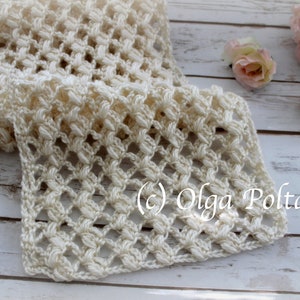 May include: A cream-coloured, open-weave crochet scarf. The scarf has a repeating pattern of raised stitches, creating a textured surface. The text "(c) Olga Poltava" is visible. The scarf is displayed on a light wooden surface.