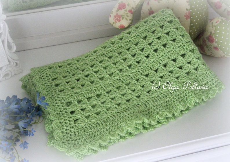 May include: A green crocheted baby blanket with a delicate, lacy pattern. The blanket has a scalloped edge and is made with a soft, lightweight yarn.
