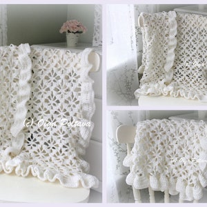 May include: A white crocheted blanket with a delicate floral pattern and ruffled edges. The blanket is draped over a white chair.