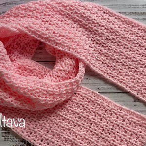 May include: A soft, light pink crocheted scarf, displayed on a wooden surface. The scarf is looped and folded, showcasing its texture and design. The name "Olga Poltava" is visible in the lower left corner.