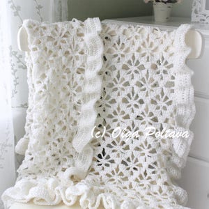 May include: White crocheted blanket with a ruffled edge, draped over a white chair. The blanket features a delicate floral pattern and is made with a soft, lightweight yarn.
