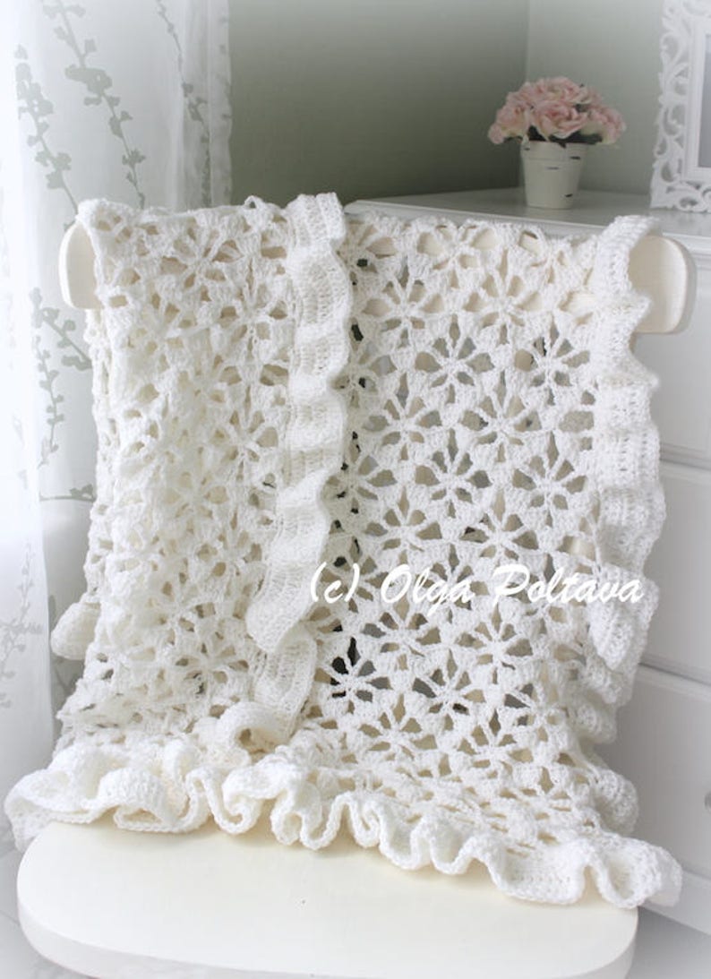 May include: White crocheted blanket with a ruffled edge, draped over a white chair. The blanket features a delicate floral pattern and is made with a soft, lightweight yarn.