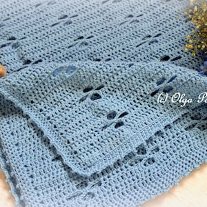 Puede incluir: Una manta de beb&eacute; de ganchillo azul claro con un delicado patr&oacute;n de punto abierto. La manta est&aacute; doblada por la mitad y tiene un aspecto suave y texturizado.