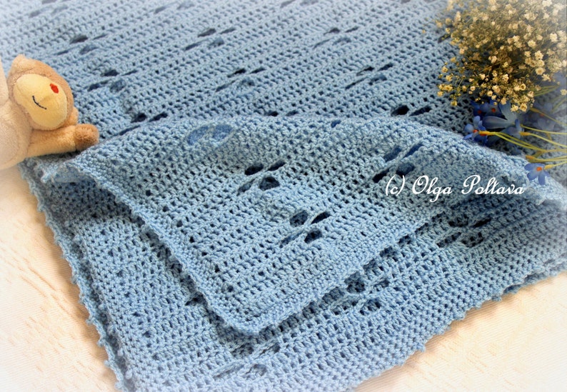 Puede incluir: Una manta de beb&eacute; de ganchillo azul claro con un delicado patr&oacute;n de punto abierto. La manta est&aacute; doblada por la mitad y tiene un aspecto suave y texturizado.