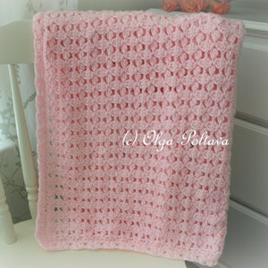 May include: A pink crocheted baby blanket with a delicate openwork pattern. The blanket is draped over a white chair.