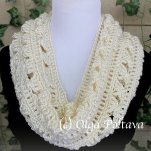May include: An off-white crochet infinity scarf featuring a textured, repeating pattern of raised stitches and openwork loops. The scarf is draped around a white mannequin neck form, displaying the intricate yarn work and cream color.