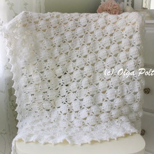 May include: A white, handmade crochet blanket with a textured pattern and scalloped edges. The blanket is draped over a chair, showcasing its intricate design and craftsmanship. The blanket is a soft, cozy home decor item.